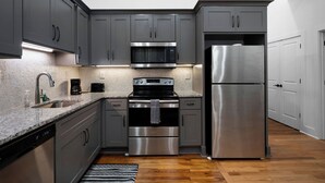 A modern kitchen with grey cabinets, stainless steel appliances, and a granite countertop. - Soho Loft 5 (Cartersville)