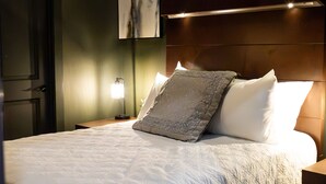 Un lit bien fait, avec une couette blanche, une tête de lit en bois et une table de chevet surmontée d’une lampe.