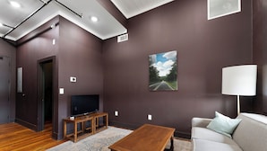 Un salon moderne avec une table basse en bois, un canapé gris, un téléviseur posé sur un meuble en bois et un tableau représentant une route accroché au mur.
