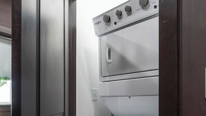 Une cuisine moderne et compacte, dotée d’un lave-linge et d’un sèche-linge intégrés, d’une porte en bois foncé et d’un interrupteur visible.