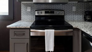 Une cuisine avec des meubles gris, un four à micro-ondes en acier inoxydable, une cuisinière et un lave-vaisselle.