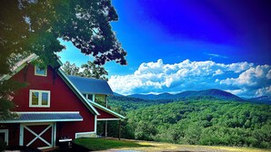 A red house with a garage, surrounded by a forested landscape and mountains in the background. - Big Mountain Views,  Minutes to Wineries, Hot Tub (Dahlonega)