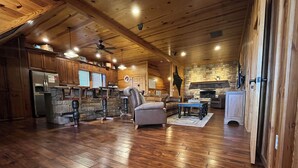 A spacious living area with a stone fireplace, wooden ceiling beams, and a stone accent wall. - Big Mountain Views,  Minutes to Wineries, Hot Tub (Dahlonega)