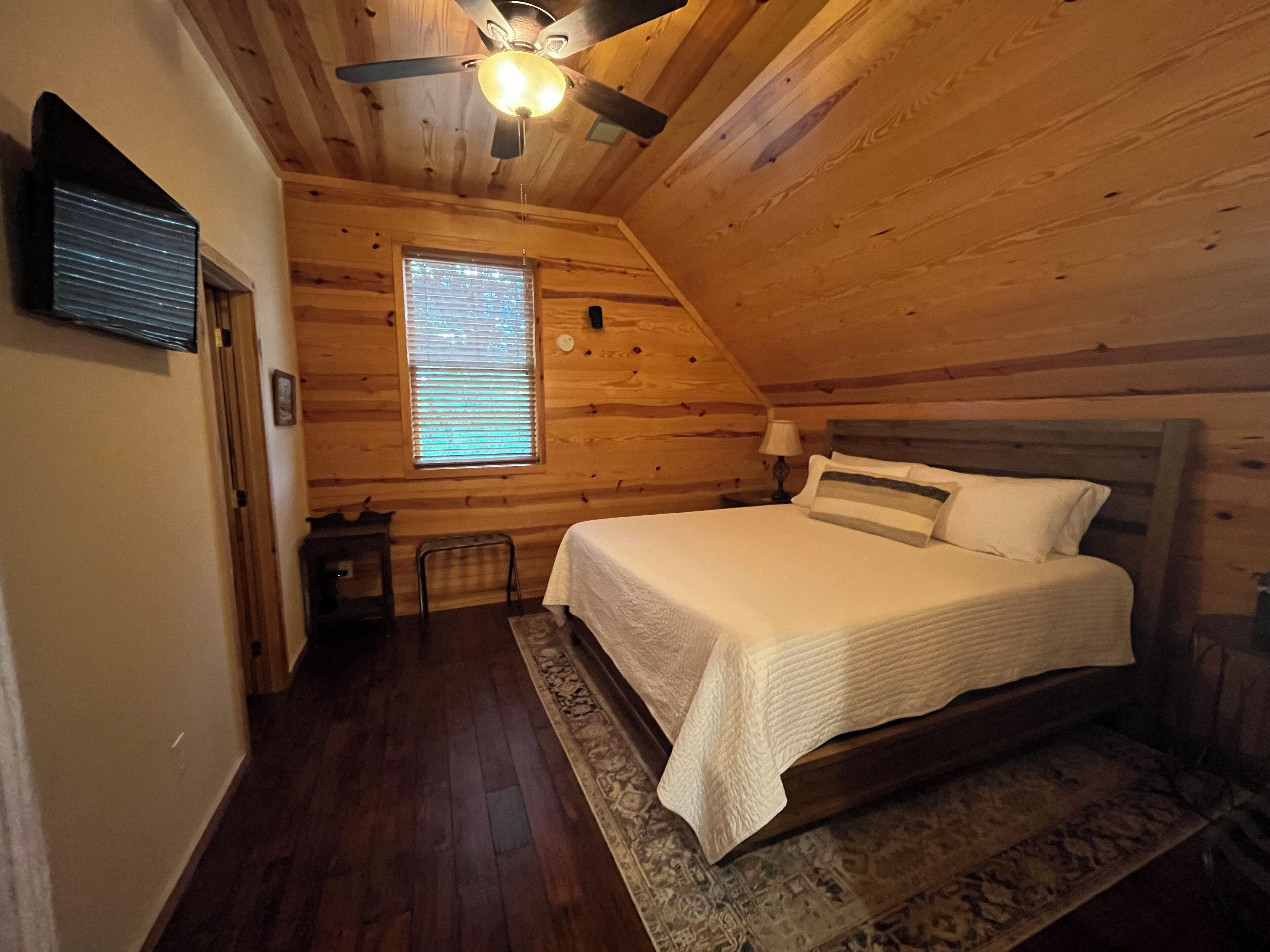 A cozy wooden cabin bedroom with a single bed, a ceiling fan, and a window with blinds.