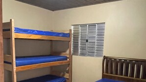 Een kamer met een stapelbed en een enkel bed, houten meubels, een raam met zonwering en een plafondventilator.