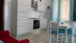 Een moderne keuken met witte kasten, een inbouwoven en een eethoek met een witte tafel en stoelen.