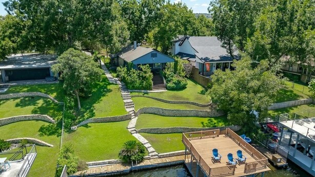 A riverside property with a dock, a wooden deck with chairs, and a house in the background.