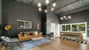 A modern living room with a dark wall, wooden flooring, a sofa, two armchairs, a coffee table, and a ceiling light fixture.
