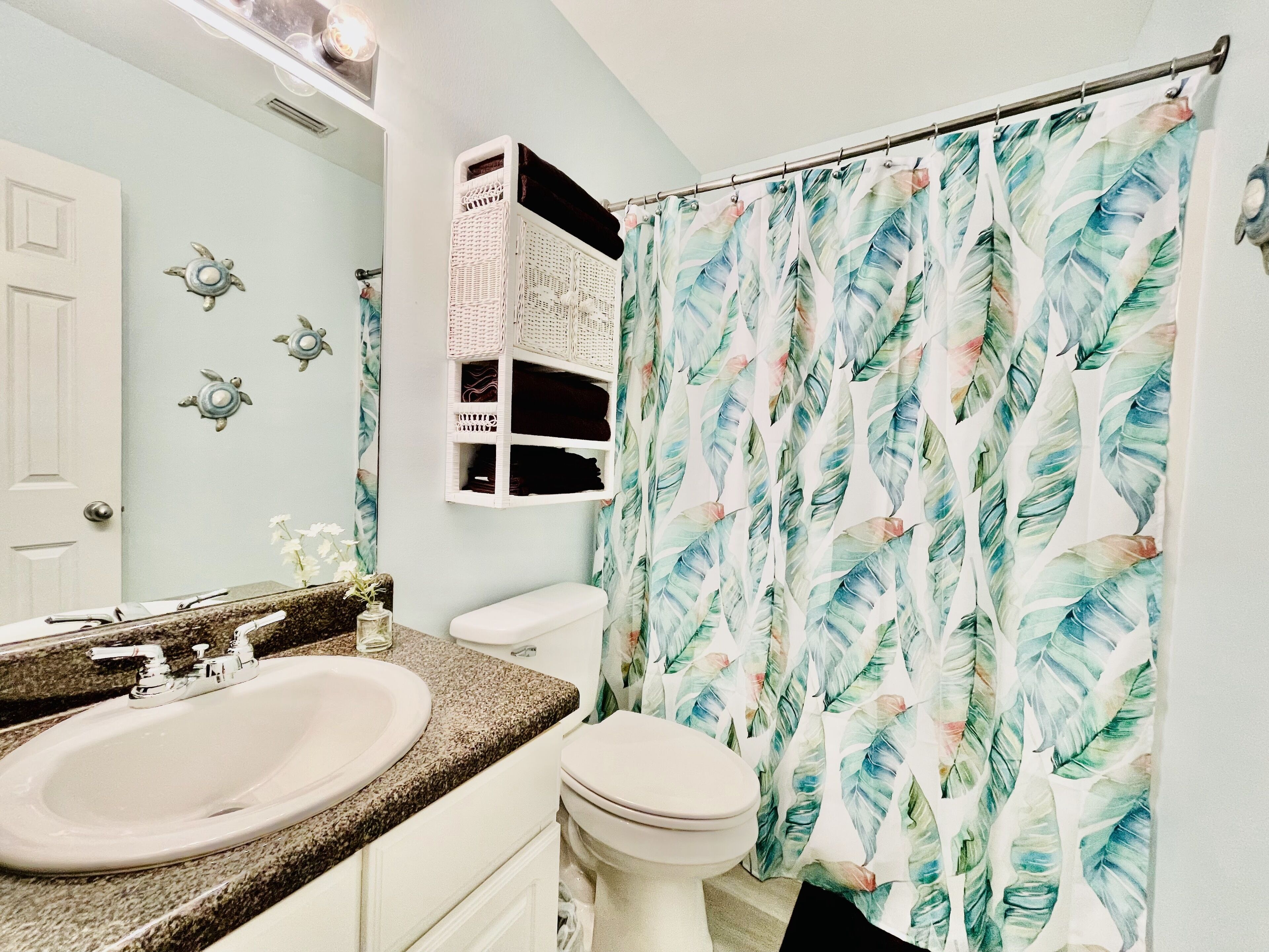 A bathroom with a white sink, a toilet, and a shower curtain with a leaf pattern.