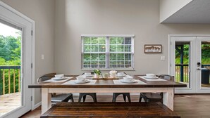 A dining area with a wooden table set for four, a window with blinds, and a view of greenery outside. - Stylish Mountain Retreat w/ Hot Tub, Games and Stunning Sunrise Mountain Views! (Sevierville)