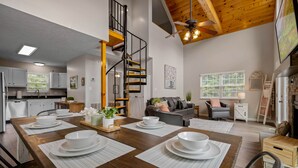 A modern kitchen with white cabinets, a wooden dining table set with white plates, and a spiral staircase leading to an upper level. - Stylish Mountain Retreat w/ Hot Tub, Games and Stunning Sunrise Mountain Views! (Sevierville)