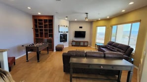 A living room with a foosball table, a leather sofa, a TV mounted on the wall, and large windows. - Custom 4 bdrm with Granny Suite and Infinity Pool (Bullhead City)