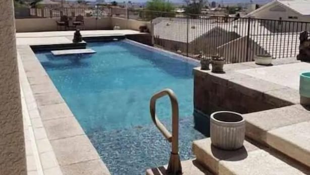 A rectangular swimming pool with a metal ladder, surrounded by stone steps and a metal fence. - Custom 4 bdrm with Granny Suite and Infinity Pool (Bullhead City)