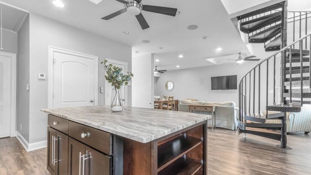 A spacious kitchen with a marble island, wooden cabinets, and a ceiling fan.