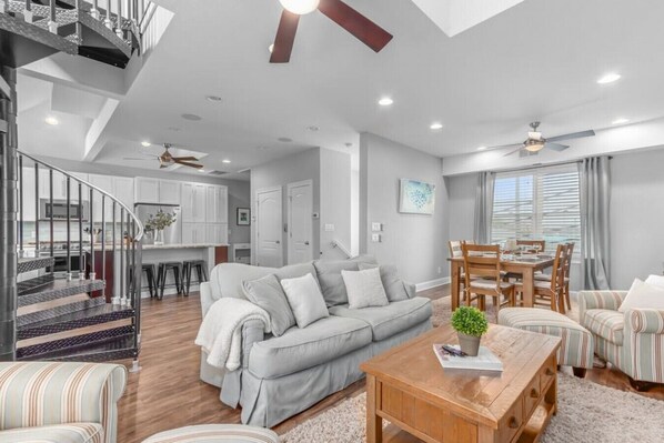 A modern living room with a grey sofa, striped armchairs, a wooden coffee table, and a staircase with a metal railing.