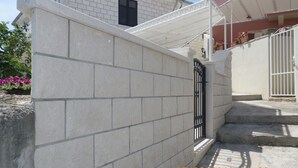 A building with a beige stone wall, a black gate, and a white staircase with a canopy. - S 2 - modern studio, just 50m from the beach (Korcula)