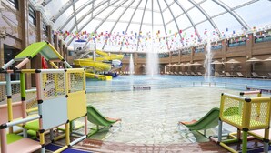 Parque acuático interior con toboganes, piscina y una zona cubierta con banderas.