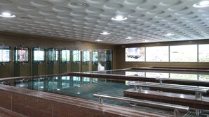 Una piscina con piso de baldosas y barandilla de vidrio. Varias ventanas exhiben obras de arte y ofrecen vista a la vegetación circundante.