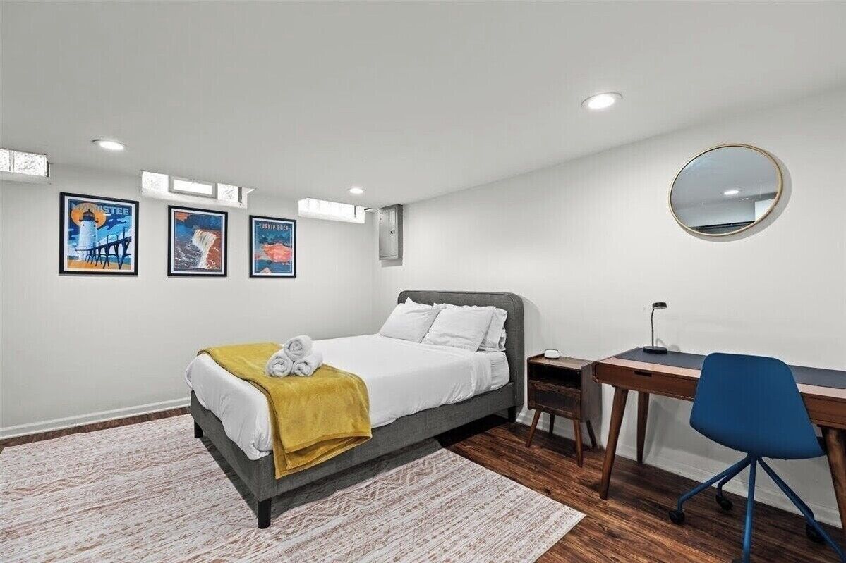 A bedroom with a bed, a desk, and a chair. There are three framed pictures on the wall.