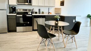 A modern kitchen with white cabinets, a built-in microwave, a stove, and a dishwasher. There is a round table with two chairs and a potted plant on the counter. - Stylish King 1BR Near MetLife & NYC (Elizabeth)