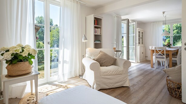 Um quarto amplo com uma grande janela, uma cadeira branca, uma mesa de jantar e uma estante de livros.