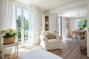 Una habitación amplia con un gran ventanal, una silla blanca, una mesa de comedor y una estantería.