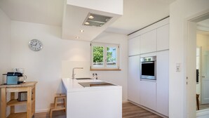 Cozinha moderna com ilha central, forno embutido e janela com vista para vegetação.