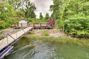 Eine Holzbrücke über einem ruhigen Fluss, umgeben von üppigem Grün und einer Steinmauer.