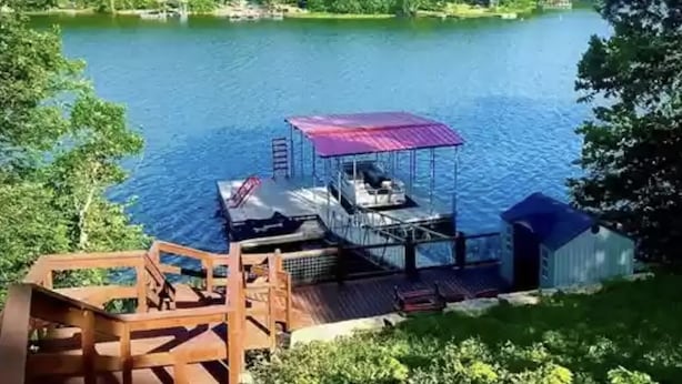 Un muelle con una zona de estar cubierta y un edificio pequeño, con vista a un lago tranquilo rodeado de árboles.