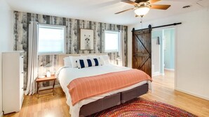 Un dormitorio con cama, ventilador de techo, ventana, puerta y pared de madera.