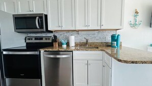 A compact kitchen with white cabinets, stainless steel appliances, and a granite countertop. - Seawatch Resort - King Bed (Myrtle Beach)