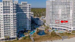 A high-rise hotel with multiple balconies, a central courtyard with a pool, and a view of the surrounding landscape. - Seawatch Resort - King Bed (Myrtle Beach)