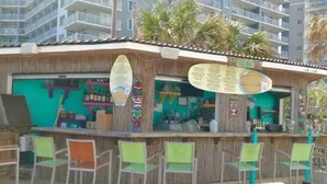 A beachside bar with a wooden exterior, a green awning, and several chairs. - Seawatch Resort - King Bed (Myrtle Beach)