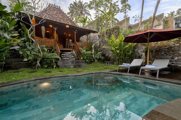A pool area with lounge chairs, a wooden structure with a tiled roof, and lush tropical vegetation. - Bubu Mesari Ubud Villa (Ubud)