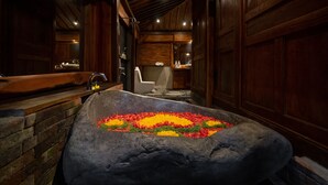Una bañera de piedra con un arreglo floral, paredes de madera, un muro de ladrillo y un espejo.