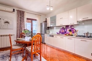 Une cuisine moderne avec des meubles blancs, un coin repas doté d’une table et de chaises en bois, et une vue sur l’extérieur par une fenêtre.