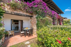 Ein Steingebäude mit überdachter Terrasse, Sitzgelegenheiten im Freien und üppiger Bepflanzung.