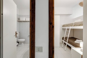 Ein kleines, kompaktes Zimmer mit einem Etagenbett, einer weißen Toilette und einem Regal mit weißen Behältern.