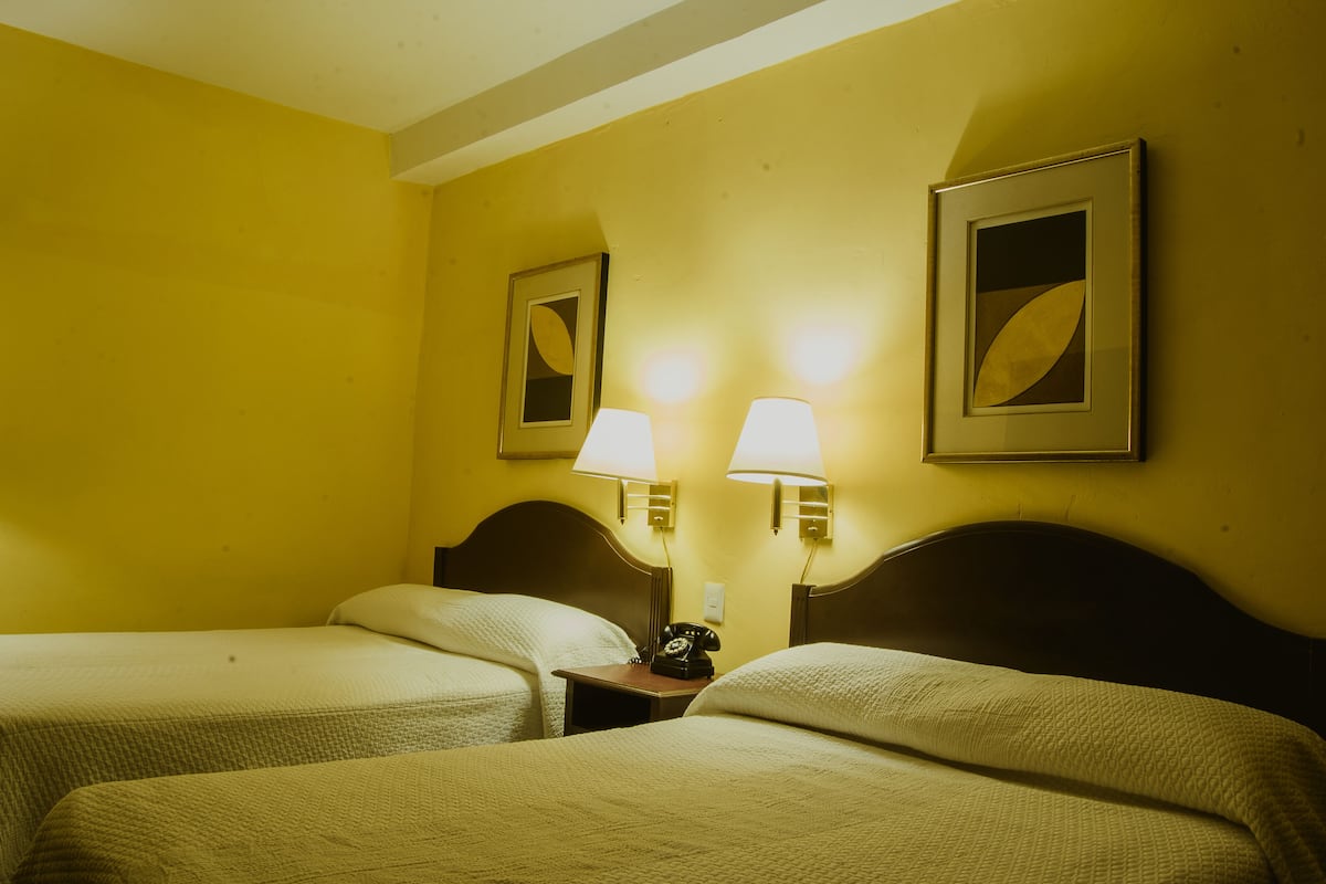 Habitación de hotel con dos camas, una mesita de noche con teléfono y dos lámparas de pared.