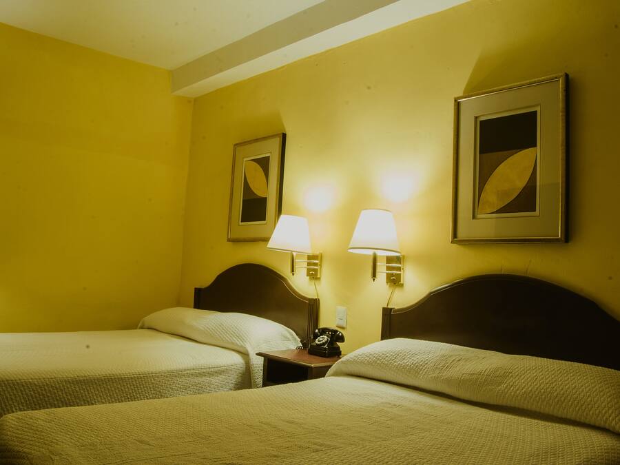 A hotel room with two beds, a nightstand with a telephone, and two wall-mounted lamps.