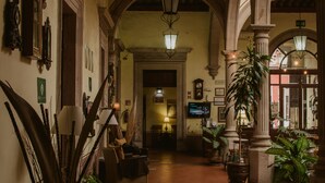 A corridor with a tiled floor, a sofa, a lamp, and potted plants. - Hotel Posada San Agustin (Durango)