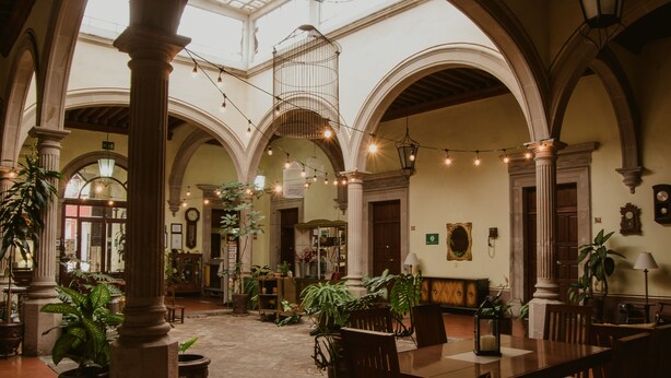 A spacious courtyard with arches, potted plants, and a wooden table and chairs. - Hotel Posada San Agustin (Durango)