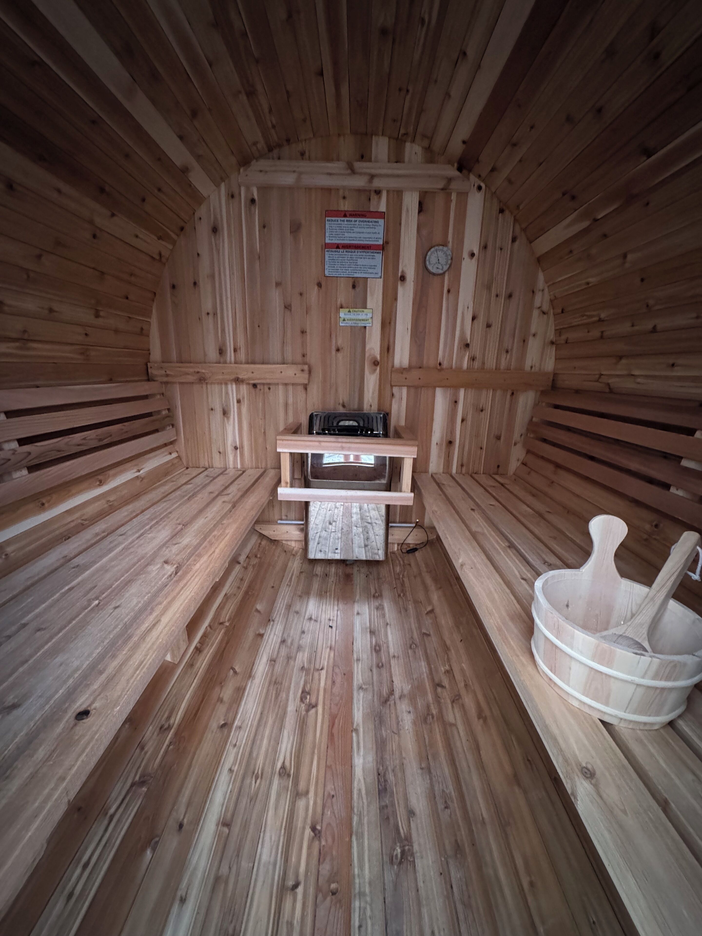 A sauna with wooden walls and benches, a heater, and a wooden bucket with a ladle.