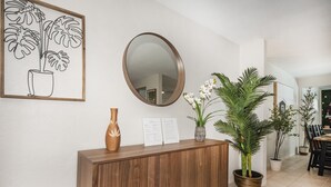 A wooden console table with a mirror, a framed plant illustration, and a vase with white flowers.