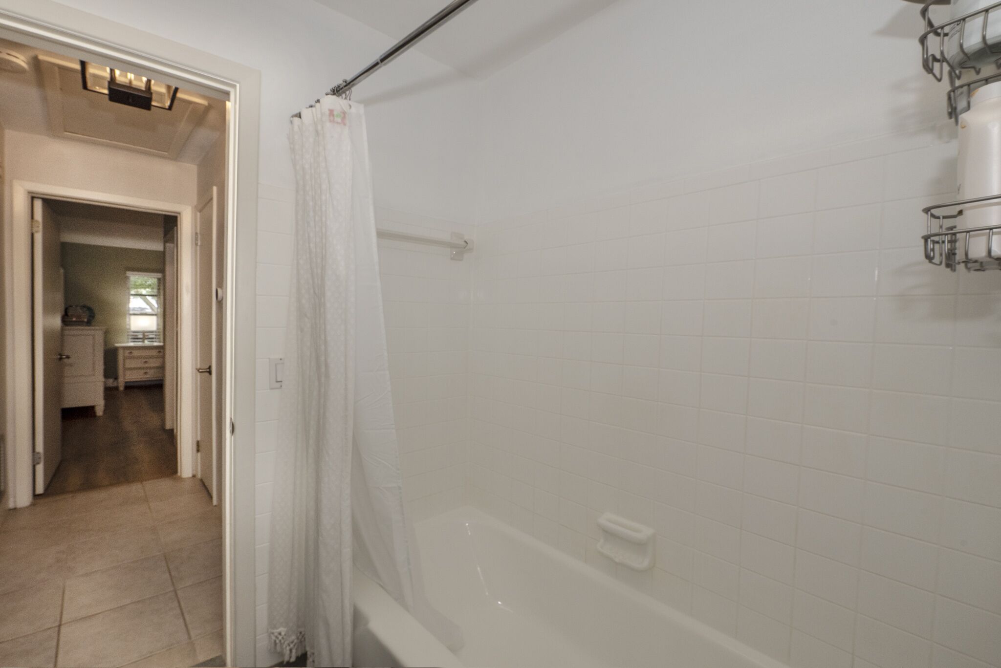 Une salle de bain avec des murs recouverts de carreaux blancs, une baignoire et un rideau de douche.