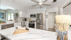 A modern kitchen with white cabinetry, stainless steel appliances, and a marble countertop.