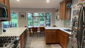 Una cocina moderna con armarios de madera, un refrigerador de acero inoxidable y una zona de comedor con mesa y sillas.