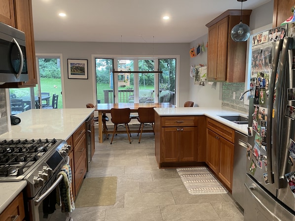 A modern kitchen with wooden cabinets, a stainless steel refrigerator, and a dining area with a table and chairs.