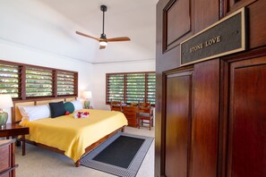 A hotel room with a bed, a desk, a chair, a ceiling fan, and a sign that reads 'STONE LOVE'.