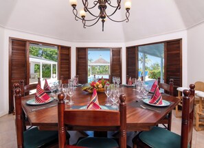 A dining area with a round table set for six, surrounded by wooden chairs with cushioned seats. - Ultra-private villa on the fairway at world-famous Tryall Golf Club. (Sandy Bay)